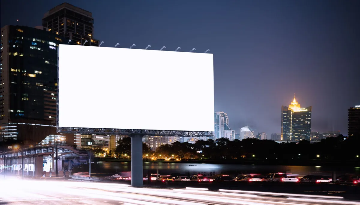 Outdoor em branco iluminado à beira de avenida, com prédios ao fundo